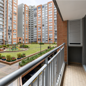 Picture of a balcony with a courtyard and other apartment buildings in the background. The courtyard has a grass lawn and a playground. A place where Shared Housing could work.